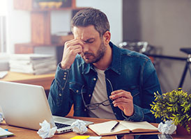 Gestresster Mann am Laptop fasst sich an die Stirn