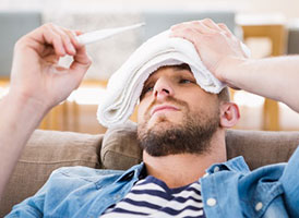 Mann mit feuchtem Handtuch auf der Stirn liest ein Thermometer ab