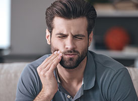 Mann mit Zahnschmerzen greift sich an die Wange